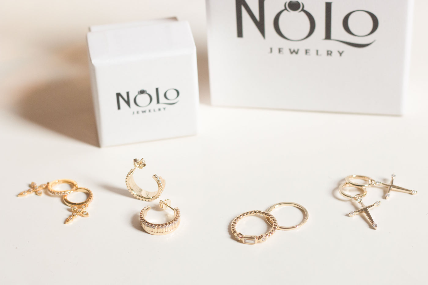 nolo jewelry signature gold cross earrings rings hoop earrings and jewelry box on white background