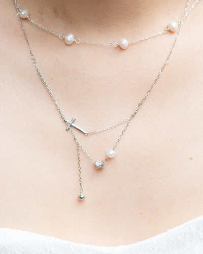 woman wearing dainty cross and pearl double layered silver necklace